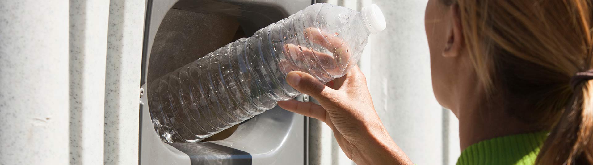 Photo d'une femme qui dépose une bouteille en plastique dans un conteneur réservé au tri du plastique